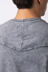 Remera oversize de algodón pesado, color gris oscuro con efecto lavado 'snow' que le da un aspecto gastado y único. Presenta cuello redondo y costuras vistas en hombros y mangas.