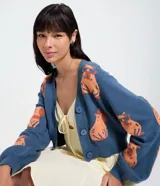 Cardigan de punto azul con escote en V, botones frontales y mangas largas ligeramente abullonadas. Presenta un estampado jacquard de carpinchos en color naranja.