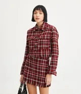 Campera corta de tweed a cuadros en tonos rojo, blanco y negro. Tiene cuello clásico, cierre frontal con botones, dos bolsillos en el pecho y flecos en el dobladillo.