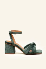Sandalia de terciopelo verde con taco cuadrado de 7 cm, punta cuadrada y tiras anchas anudadas en el empeine. Cuenta con una tira fina ajustable al tobillo con hebilla dorada.