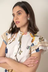Vestido midi camisero de algodón color natural con estampado de flores, animales y ramas en tonos rojo, marrón, verde y azul. Tiene cuello mao, mangas cortas con volados, bolsillos laterales y cinturón de soga color beige.
