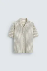 Camisa de hombre relaxed fit confeccionada en tejido de algodón a rayas verticales blancas y negras. Tiene cuello bowling, manga corta, bajo con aberturas laterales y cierre frontal de botonadura.