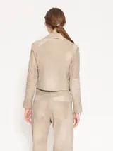 Chaqueta de cuero ovino color beige, con cuello clásico, cierre cruzado y múltiples bolsillos con cierre metálico. Presenta canesú y recortes matelaseados en codos.