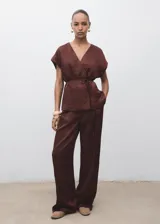 Pantalón de vestir de tiro medio, color marrón oscuro, con efecto arrugado en la tela satinada. Presenta un diseño recto, pinzas delanteras y cierre oculto.