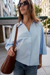 Camisa blanca de popelín con cuello solapa, escote en pico, manga ancha con vuelta y cierre frontal con botones.