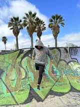 Canguro negro con capucha y cordones ajustables. Estampa en la espalda con el texto "Chema Surf Trip" y dibujos de un sol, una tabla de surf, una carpa y otros elementos relacionados con el surf.