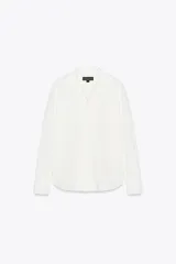 Camisa blanca de algodón con cuello solapa, manga larga con puños abotonados, bolsillo de parche en el pecho, bajo redondeado y cierre frontal con botones.