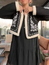 Chaqueta corta negra con interior de piel sintética color crema. Presenta bordados florales blancos en el frente y ribete de piel sintética en cuello, puños y ruedo.