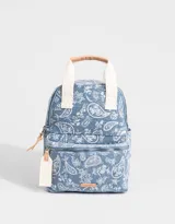 Mochila de denim azul con estampado paisley blanco, bolsillo frontal con cierre, correas regulables y manijas superiores de algodón con broche de cuerina. Acceso mediante cierre superior y puller de cuerina. Incluye tag de cuerina.