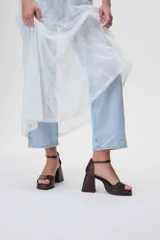 Sandalias de cuero negro con plataforma y tacón cuadrado alto. Presentan una tira delgada sobre los dedos y pulsera tobillera con hebilla dorada.