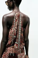Vestido largo con estampado cachemir en tonos marrones, cuello halter con cordones con abalorios, nido de abeja elástico en la cintura, forro interior y tejido con hilo metalizado.