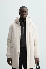 Parka color crudo de tejido técnico acolchado, con cuello alto y capucha ajustable. Tiene mangas largas con puños ajustables, bolsillos frontales con solapa, bolsillo interior y cierre frontal con cremallera oculta por solapa con botones a presión.