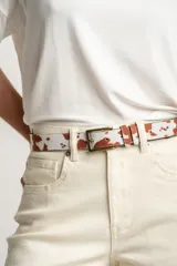 Cinto de cuero con estampado de vaca en tonos marrones y blancos, hebilla metálica color bronce.