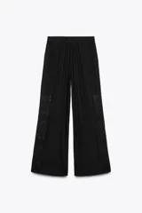 Pantalón negro con bordados florales en los laterales, tiro alto, cintura elástica en la parte trasera, bolsillos laterales, pliegues y cierre frontal con cremallera, botón interior y gancho metálico.