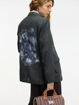 Blazer gris oscuro de lana con cuello solapa y cierre con botones. Presenta pedrería decorativa en la parte delantera y trasera.