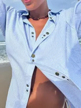 Camisa celeste y blanca a rayas verticales, con botones metálicos a presión, corte relajado y cuello clásico.