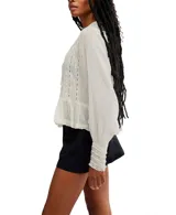 Blusa color crema de voile semitransparente con cuello y mangas largas con ribete de encaje, y botones en el frente.