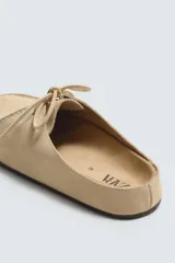 Zueco color beige de piel con acabado serraje, detalle de cordones y bordón en el empeine, plantilla acolchada, horma redonda y suela ultrafina a contraste.