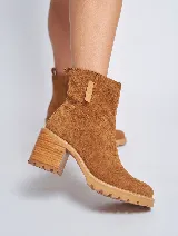 Bota corta de gamuza color marrón, con taco cuadrado de madera y suela track. Presenta un tirador en la parte posterior. Confeccionada 100% en cuero genuino.