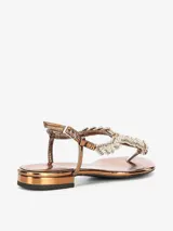 Sandalia color bronce con tira en el dedo y diseño entrelazado con apliques de strass. Cuenta con pulsera ajustable en el talón y una base plana de leve altura.