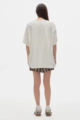 Remera unisex color crudo, de cuello redondo y manga corta, con estampado frontal de una figura humana y texto en dorado.