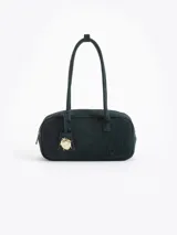 Cartera rectangular de estructura firme confeccionada en cuero descarne vacuno color marrón. Presenta manijas fijas, cierre superior y un charm metálico dorado en forma de vaquita de San Antonio colgando de un tag lateral. Incluye el logo de la marca grabado en relieve en el frente.