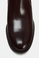 Botín de cuero color marrón oscuro, estilo Chelsea, con elásticos laterales, hebilla decorativa en la caña, tirador trasero y tacón bajo cuadrado.