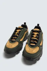 Zapatillas deportivas color crema con cordones, suela gruesa con diseño irregular y detalles en gris.