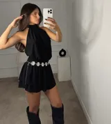 Vestido corto negro con escote halter, cintura elástica y falda con volados. Incluye un cinturón de cadena plateada con dijes redondos.