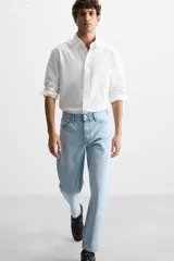 Pantalón de jean celeste de corte slim fit y tapered, con cinco bolsillos, efecto lavado y cierre frontal con cremallera y botón.
