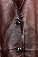 Blazer de cuero color marrón chocolate con cuello solapa, cierre frontal con dos botones, bolsillos de vivo y abertura en la espalda.