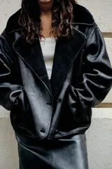 Cazadora negra de cuero sintético con cuello solapa y manga larga. Tiene bolsillos de plastrón en delantero, interior de borreguillo combinado a tono y cierre frontal con botones.