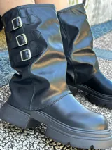 Botas de caña media de cuero sintético negro con suela track y tres hebillas decorativas.