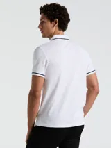 Polo blanco de piqué de algodón, corte clásico, manga corta con ribete azul marino, cuello con ribete azul marino, tapeta de dos botones y bolsillo de parche en el pecho con logo bordado.