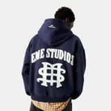 Hoodie azul marino con capucha y cordón ajustable, corte oversize y puños y cintura acanalados. Estampado frontal y trasero con el nombre de la marca y un símbolo gráfico.