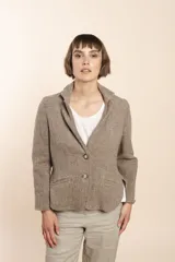 Chaqueta color crema de corte recto con cuello, solapa y bolsillos ojal. Forro solo en las mangas y terminaciones envivadas. Esquinas redondeadas y mangas con corte en puño que permiten transformarla en manga 3/4. Más larga en la espalda que en la delantera. Abrochadura con dos botones.