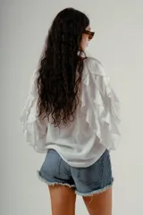Blusa blanca de manga larga con volados en los puños y escote en V con botones frontales.
