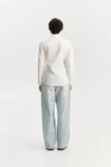 Camisa blanca de manga larga con cuello camisero, bolsillo frontal superior y tiritas ajustables en los costados para atar en la cintura.