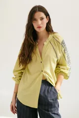 Camisa blanca de manga larga con bordados marrones en hombros y mangas, cuello en V y cierre frontal con botones.