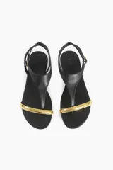 Sandalias planas negras con tira delantera y pulsera al tobillo, detalle de aplique metálico dorado en la puntera.