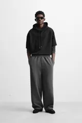 Pantalón jogger wide fit color gris oscuro, confeccionado en tejido de algodón compacto con elasticidad. Cuenta con cintura elástica ajustable con cordón, pliegues frontales, bolsillos delanteros y bolsillo trasero de parche.