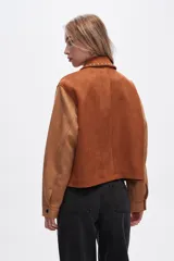 Chaqueta corta color marrón con detalles en color camel, de gamuza sintética, con cuello camisero, cierre frontal con cremallera y apliques de tachas plateadas.