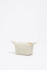 Monedero trapecio de tamaño mini, color crudo, con cierre dorado y logo de la marca estampado en dorado.