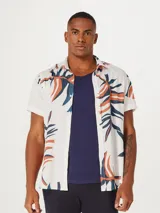 Camisa blanca de manga corta con estampado de hojas en negro y gris. Tiene cuello clásico y cierre frontal con botones. Corte recto.