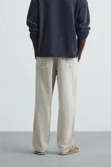 Pantalón color arena de corte recto, confeccionado en tejido de algodón y lino. Cuenta con cintura elástica ajustable con cordón, bolsillos delanteros y traseros de parche.