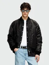 Campera bomber negra de hombre, estilo aviador, con cuello y puños acanalados. Presenta cierres metálicos visibles y bolsillos frontales con solapa y broche.