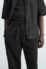 Pantalón negro de corte amplio, con textura acanalada, cintura elástica ajustable con cordón, bolsillos laterales y traseros de vivo.