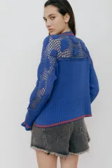 Cárdigan azul con detalles en crochet, mangas con volado y vivos de color rojo en cuello, puños y frente. Tiene botones al frente.