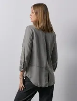 Camisa celeste de tencel con cuello con solapa, escote en V, abertura central con botones y mangas 3/4 regulables con presilla y botón.
