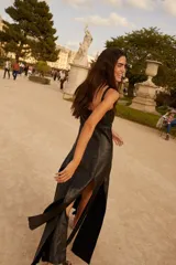 Vestido negro de cuero con tirantes anchos y escote recto. Presenta un detalle de costura decorativa con cordón azul oscuro a la altura de la cintura.